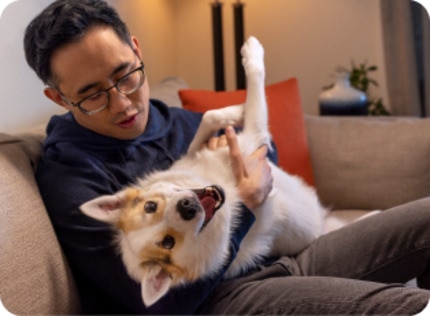 A man is sitting on a sofa with his pet dog in his arms.